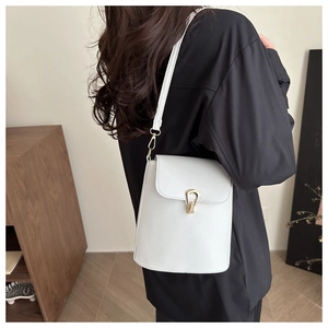 Minimalist white leather crossbody bucket bag worn on shoulder with golden metal buckle clasp
