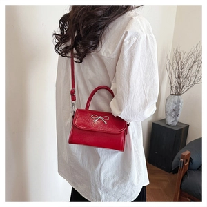 Red patent leather mini handbag with silver bow detail worn as a crossbody bag