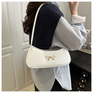 Detail of white PU leather baguette bag with golden metal bow buckle on model