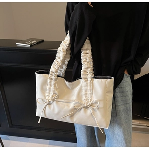 White nylon tote bag with pleated handle and double bow detail shown on a shoulder
