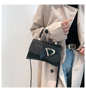 Close-up of a black sequined box handbag with a gold D-buckle worn with a beige coat