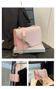 Detail of pink crossbody bag with woven texture flap, metal bar, and gold chain strap