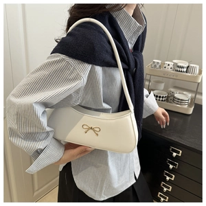 Detail of white leather shoulder bag featuring a gold bow accent and half-moon design