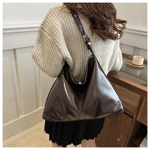 Detail of a large chocolate brown patent leather tote bag with adjustable wide strap