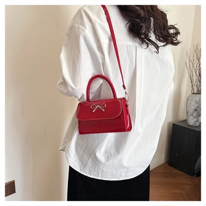 Detail of red patent leather square handbag with silver bow accent on model