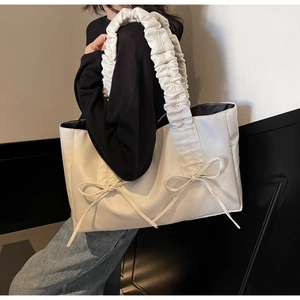Close-up of pleated shoulder strap and ribbon bow detail on cream nylon tote bag