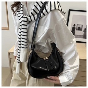 Detail of glossy black crescent hobo bag with gold dual zippers on a model in a warm setting