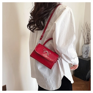 Detail of red glossy patent leather handbag with silver metal bow and magnetic flap