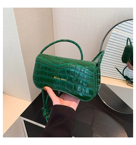 Detail of dark green crocodile texture on a patent leather shoulder bag with gold logo
