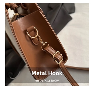Detail of a brown leather bag showing the golden metal hook and shoulder strap stitching