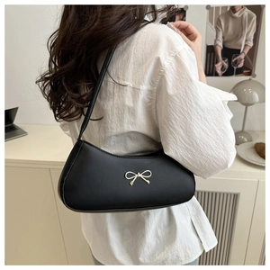 Detail of vintage black leather baguette bag with golden bow buckle on model shoulder