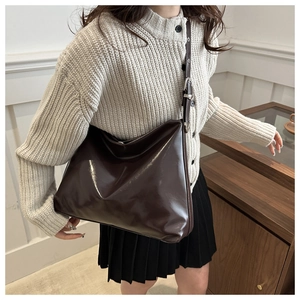 Détail d'un grand sac cabas marron brillant avec bandoulière porté par un modèle
