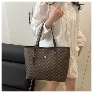 Braune Monogramm-Einkaufstasche mit goldenem M-Logo an Model in weißem Spitzenkleid