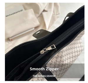 Close-up of smooth metal zipper and monogram print on cream tote bag detail