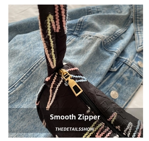 Detailed macro view of the gold metal zipper on a black jacquard nylon dumpling bag