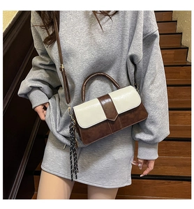 Sac bandoulière bicolore marron et blanc avec pompon sur des escaliers en bois