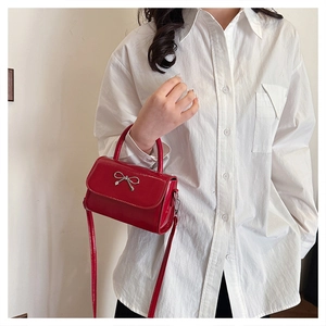 Detail of red glossy crossbody bag with silver metal bow and long shoulder strap