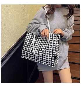 Fashionable large black and white houndstooth tote bag worn on shoulder by a model