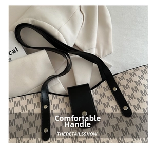 Detail of gray monogram tote bag with black leather handle and silver metal rivets