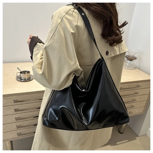 Close-up of a glossy black patent leather tote bag featuring sleek side buckle details