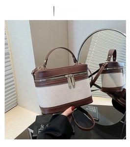 Detail of two-tone bucket bag with beige weave and brown leather trim and golden zippers