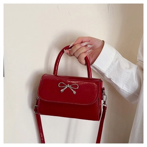 Close-up of red patent leather square bag with silver metal bow and shiny finish