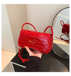 Detail of red crocodile texture handbag with gold logo and knotted strap accents