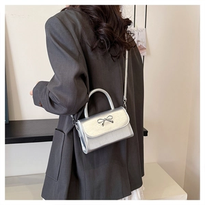 Silver mini crossbody bag with metal bow detail worn by model in a modern interior