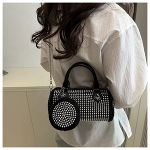 Detail view of black cylinder bag featuring silver studs and small round coin purse charm