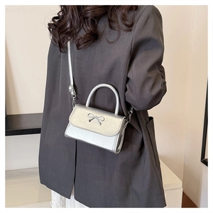 Silver metallic crossbody bag with bow buckle worn over a grey blazer and white dress