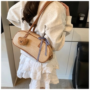 Minimalist straw woven shoulder bag with leather straps and bear charm shown on model