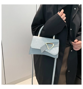 Detail of glittery crossbody bag with gold D-buckle shown on a model in black coat
