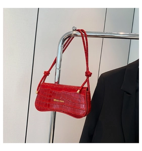 Close-up of a glossy red crocodile-embossed mini baguette bag with gold lettering details