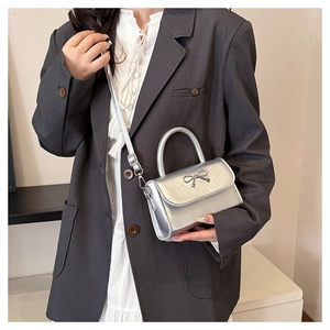 Detail of silver metallic handbag featuring a metal bow buckle and round top handle