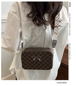Close-up of brown M-patterned crossbody bag featuring a bow buckle and woven strap