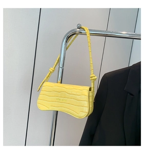 Detailed view of yellow faux crocodile leather texture and curved bottom on shoulder bag