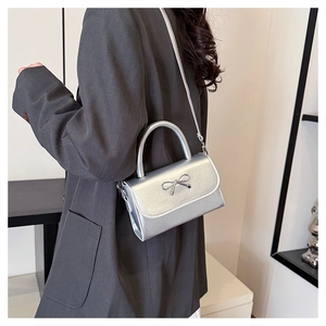 Silver square handbag with metallic bow detail shown on a model with shoulder strap