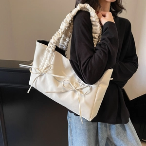 Chic cream nylon tote bag with ruched handle and bow accents on minimalist model shot