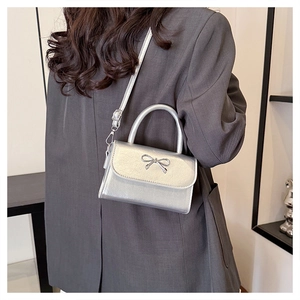 Detail of silver mini handbag with metallic bow clasp and crossbody strap on grey blazer