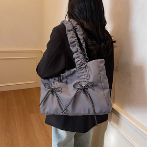 Grey nylon tote bag with black bows and ruched shoulder strap shown on a model