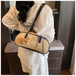 Detail view of woven straw shoulder bag with black leather trim and cute bear charm