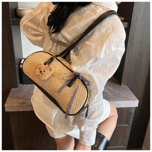 Straw cylindrical underarm bag with bear charm and bow detail shown on a model