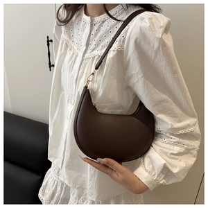 Detail of a dark brown crescent underarm bag with gold metal hardware on model