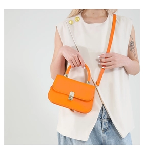 Detail of orange leather crossbody bag with metallic twist lock on model's shoulder