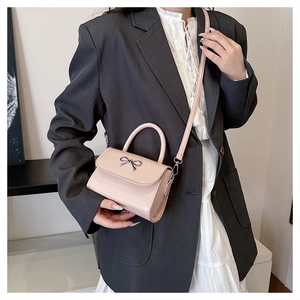 Detail of powder pink mini crossbody bag featuring a silver metal bow and leather handle
