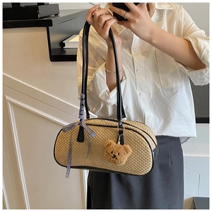 Detail of woven straw shoulder bag with black handles and a brown plush bear charm