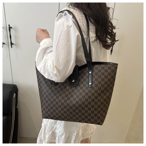Close-up detail of the large tote bag showing brown jacquard M-letter pattern and leather strap