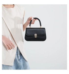 Detail of minimalist black leather saddle bag featuring premium gold metal hardware and lock