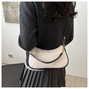 Détail du sac sous l'aisselle en cuir crème avec bord noir et chaîne dorée