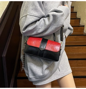 Détail d'un sac carré rouge et noir avec rabat en V, pompon et bandoulière réglable